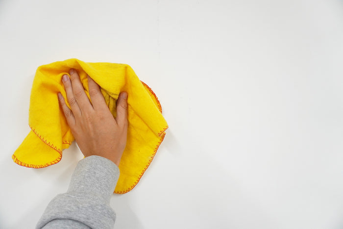 A mans hand holding a yellow cloth using it on a wall to clean it of any dirt