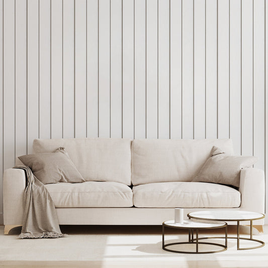 A living room with a neutral coloured sofa featuring 'Airin' which is a white wallpaper featuring vertical wooden planks with realistic wood grain and subtle weathered texture in a rustic panelled design.