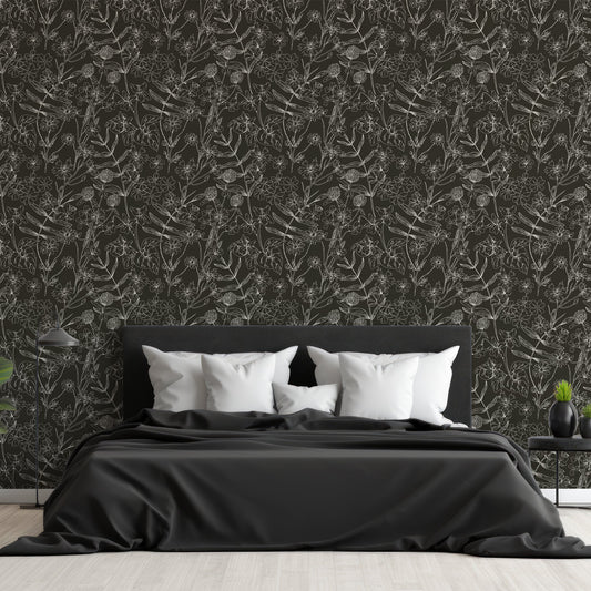 A bedroom with a black fabric bed and low side tables featuring 'Asa' which is a black and white botanical wallpaper featuring delicate outlined flowers, leaves and plant illustrations on a contrasting background in an intricate repeating pattern.
