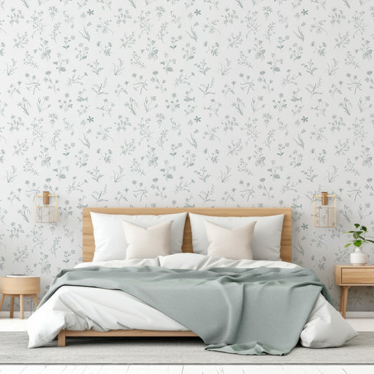 A bedroom with light coloured furnishing showing 'Nola' which is a soft vintage wallpaper featuring delicate wildflower line drawings in pastel green tones on a gentle grey background in a repeating botanical pattern.