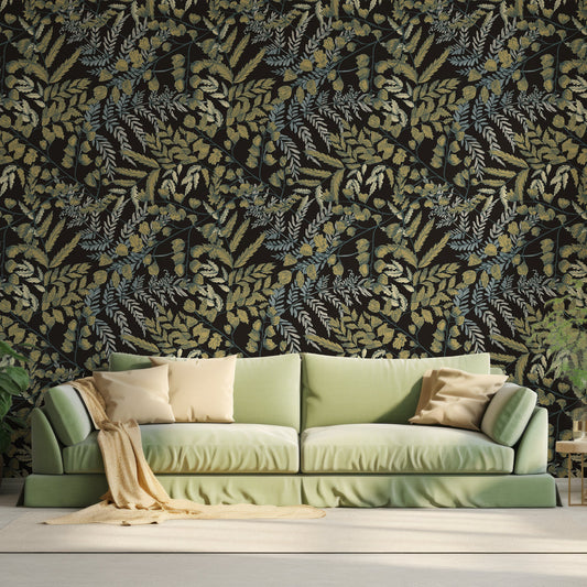 A living room with a lime green fabric sofa with butter yellow pillows and blanket across it which feaures the Ottilie wallpaper which is a vintage-style golden leaves with green foliage on a deep black background in a repeating botanical pattern.