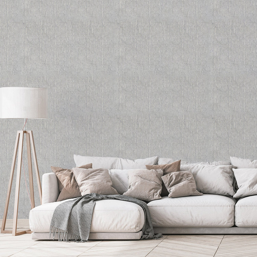 A living room with a standing lamp and white fabric sofa featuring 'Alina' which is a grey wallpaper featuring a soft wool fabric-effect texture with a woven appearance and subtle tonal variation in a minimalist repeating design.