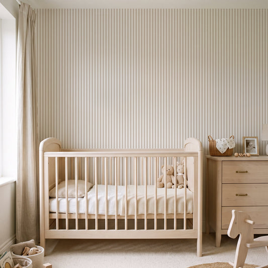 A light natural wood crib with a white mattress and bedding, styled in a bright, neutral-toned nursery with striped wallpaper, a wooden dresser, and a rocking horse.