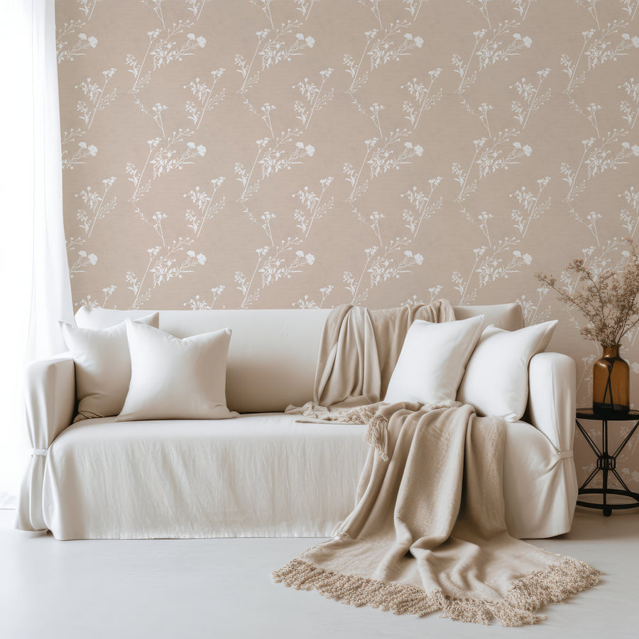 A living room with a linen fabric sofa with pillows and blankets on featuring 'Daniella' which is a minimal botanical wallpaper featuring delicate wildflower stalks and slender leafy branches on a textured neutral background in a subtle repeating pattern.
