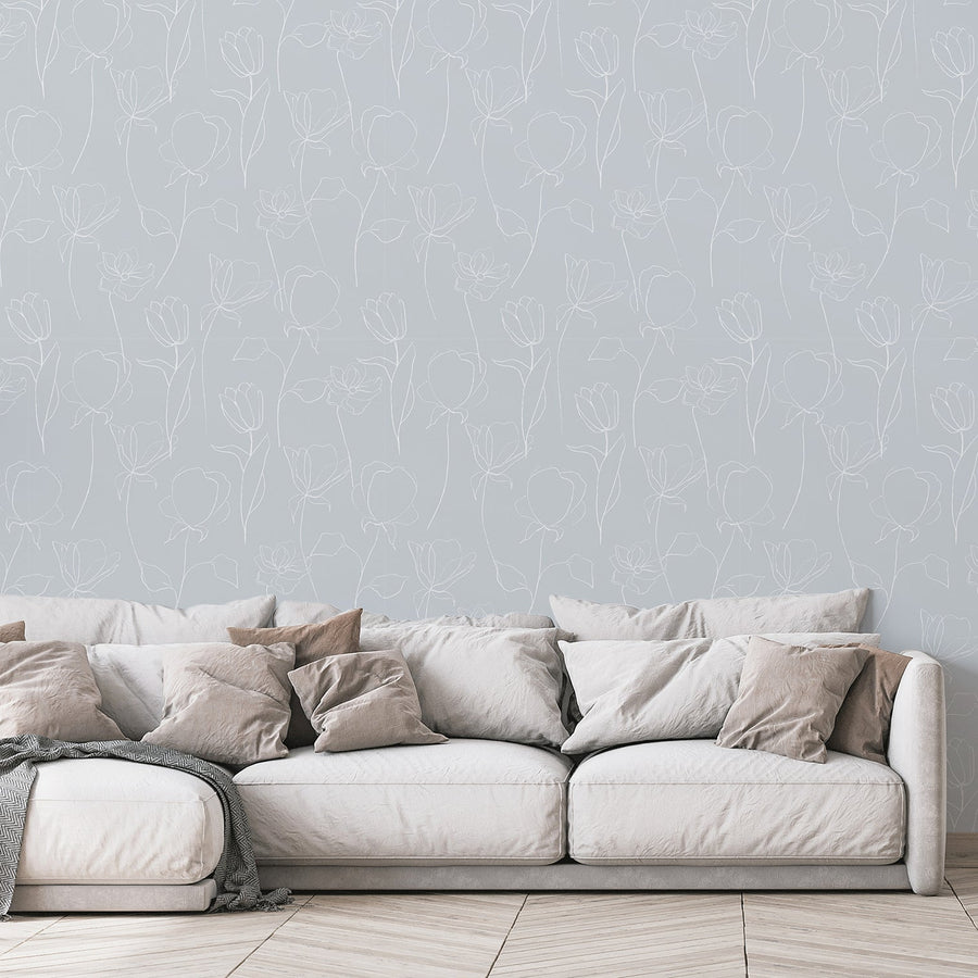 A living room with a white fabric sofa scattered with pillows featuring 'Neriah' which is a grey wallpaper featuring delicate white flower outlines and leafy botanical stems in an elegant repeating floral pattern.