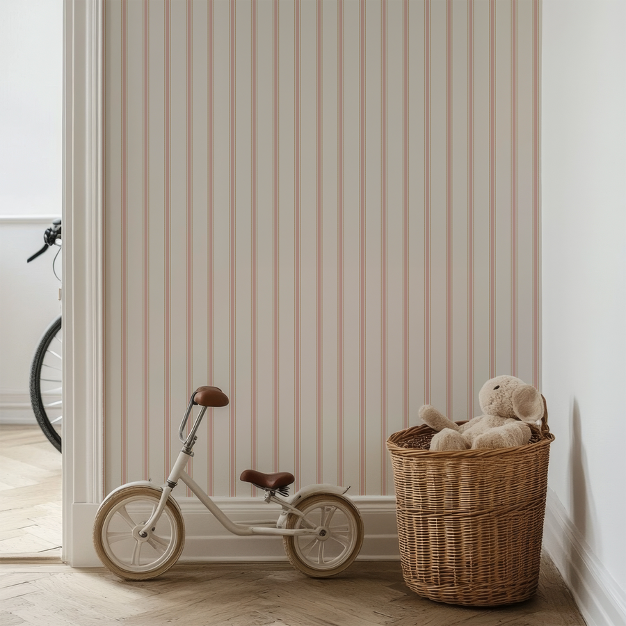 A child's room with a bicycle and wooden basket with plush toys in showing 'Grace' which is a classic striped wallpaper with thin evenly spaced vertical lines inspired by traditional ticking fabric.
