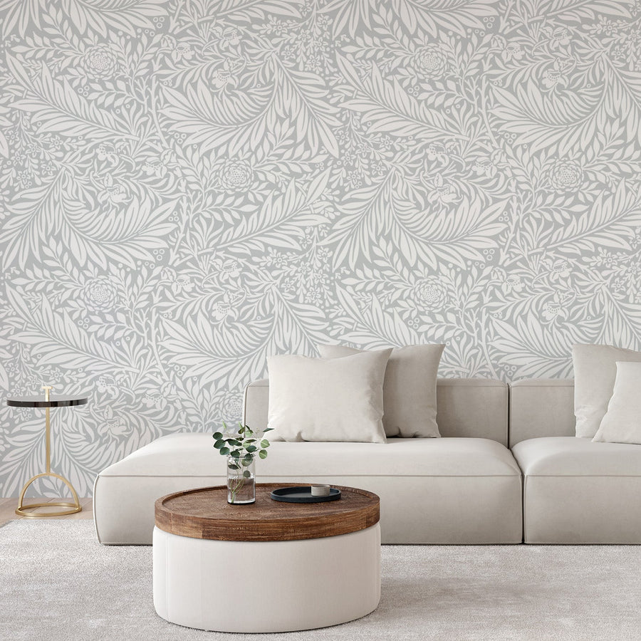A room with a light coloured sofa with a low coffee table showing 'Beatrix' which is a botanical wallpaper featuring realistic green leaves, twigs and branches arranged in a natural repeating pattern on a light background.