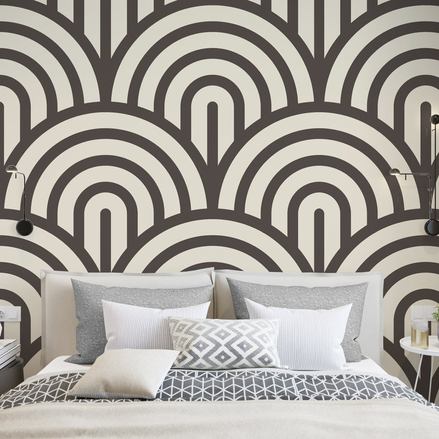A bedroom showing a modern bed scattered with cushions featuring 'Jabrielle' which is a cream wallpaper featuring bold black retro arches in a repeating geometric pattern with a subtle textured effect.