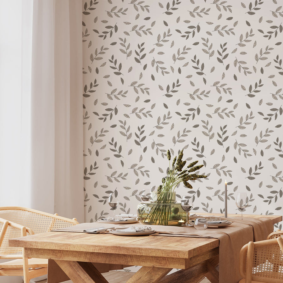 A dining room with a wooden table and chairs with plants on top of it featuring 'Llana' which is a botanical wallpaper featuring layered brown and beige tropical leaves with delicate leafy vines on a soft neutral background in a natural repeating foliage pattern.